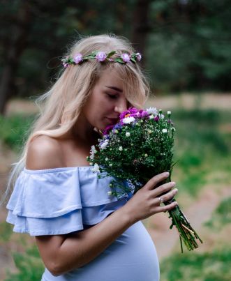 Kobieta w ciąży trzymająca swój brzuszek, wąchająca wiosenne kwiaty.