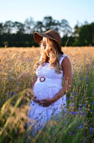 Kobieta w ciąży stojąca latem wsród zboż.