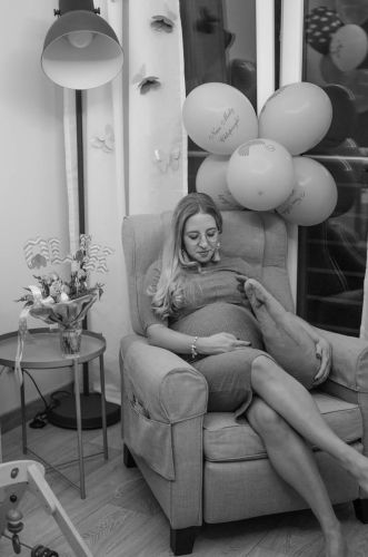 Kobieta w ciąży siedzaca w swoim pokoju i głaskająca brzuszek.