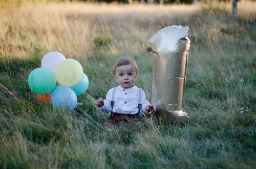 Chlopczyk obchodzacy pierwszy roczek, trzymjacy w rece balony.