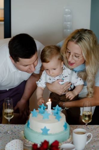 Chłopczyk z rodzicami zdmuchający świeczki z tortu urodzinowego.